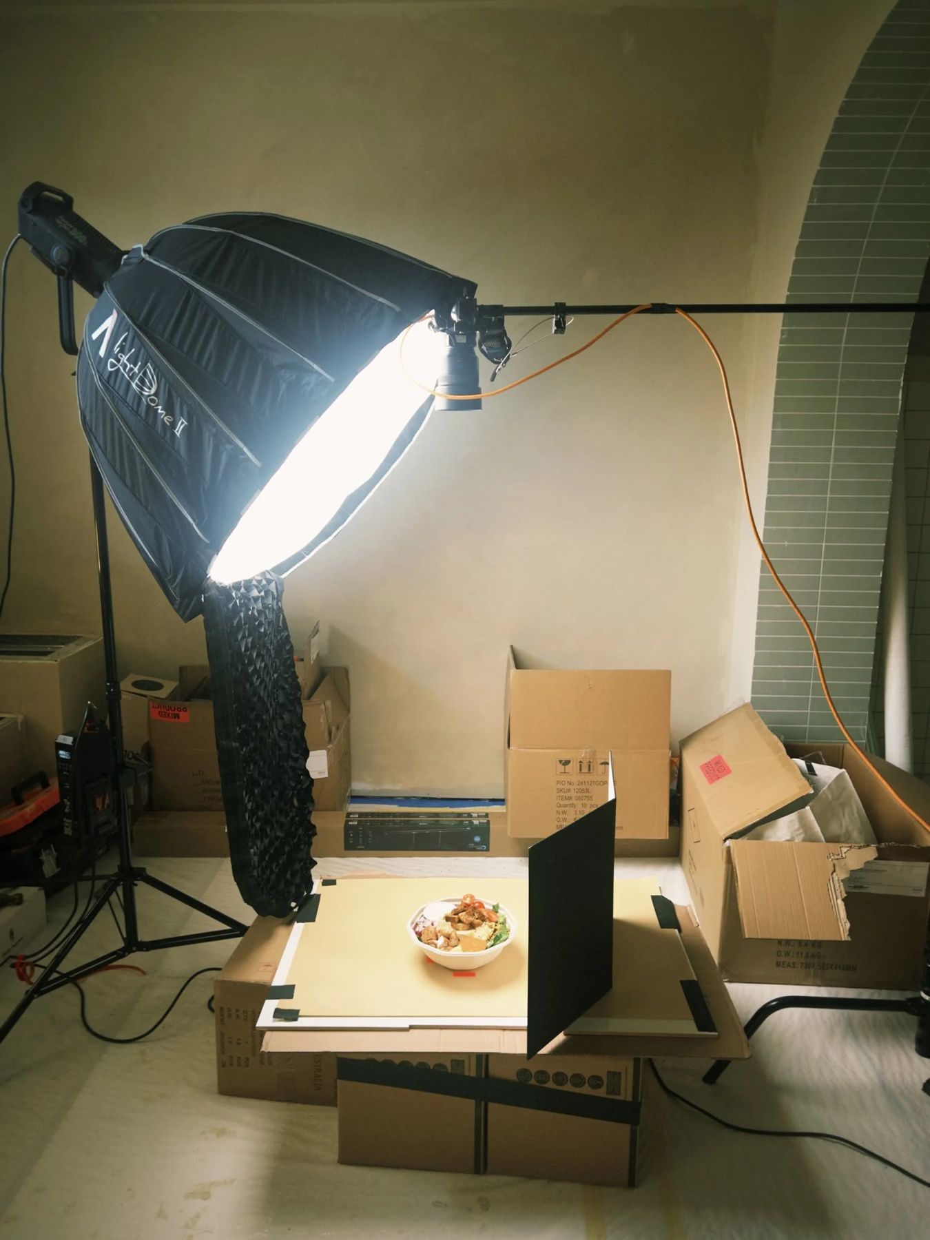 A gridded softbox rigged over a Butterleaf bowl on a paper backdrop stacked on cardboard boxes.