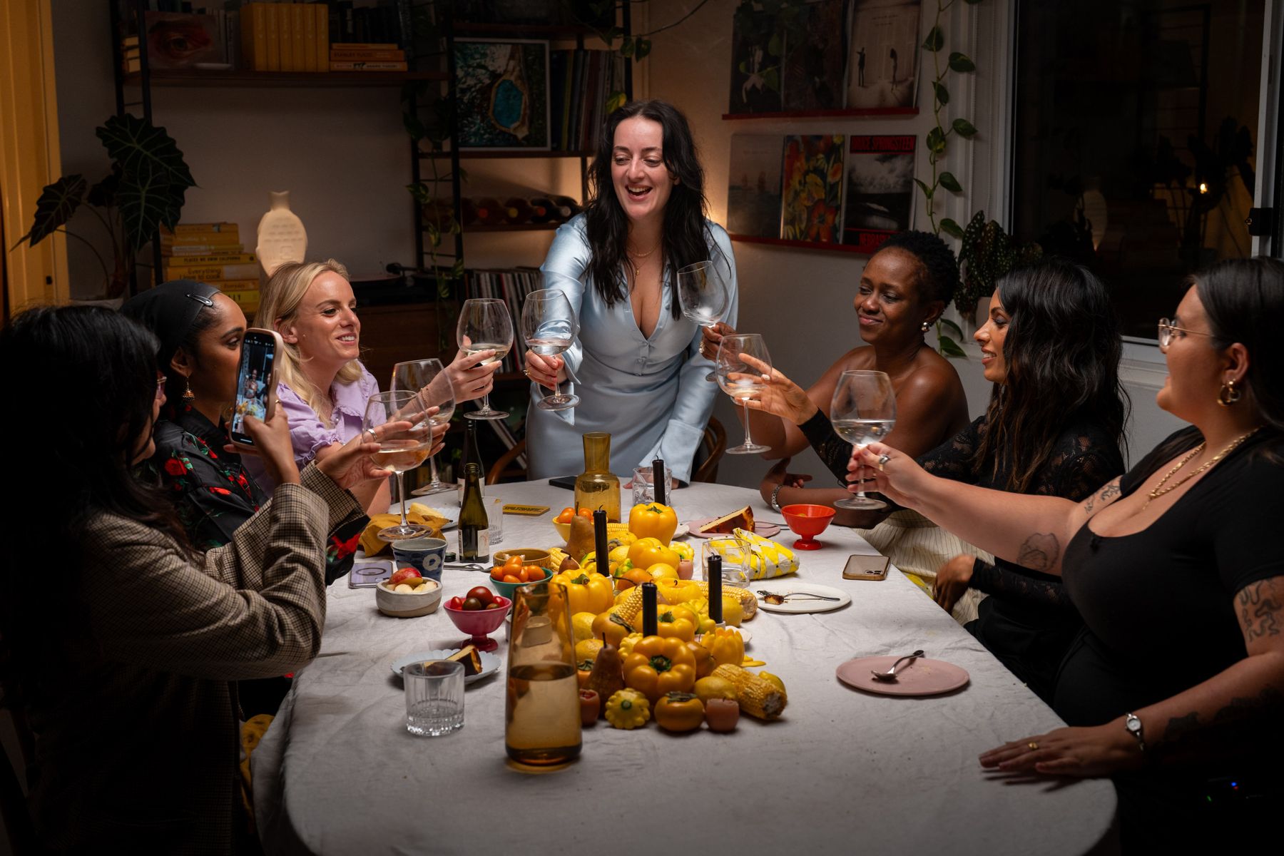 Charlotte Ree raising a glass at a candlelit dinner table styled in yellow